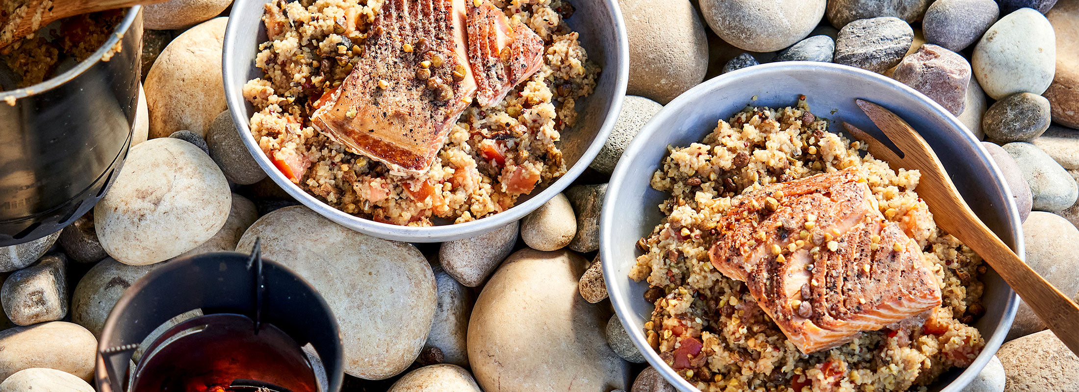 Two bowls of Patagonia Provisions Wild Pink Salmon and Savory Grains rest on a rocky beach